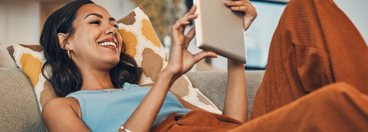 Vrouw ligt op de bank met een tablet in haar handen